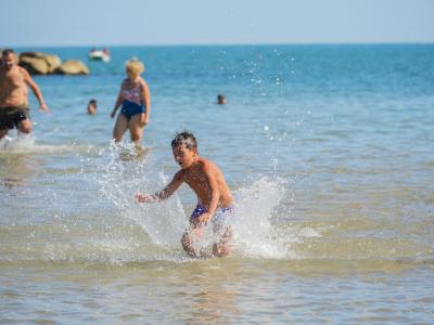 Kind spielt im Meer mit Wasserspritzern, Erwachsene im Hintergrund.