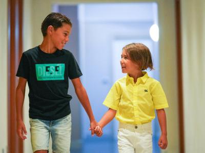 Due bambini sorridenti si tengono per mano in un corridoio.