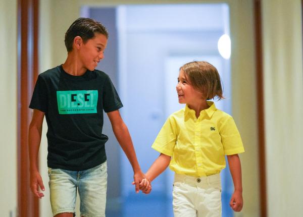 Due bambini sorridenti si tengono per mano in un corridoio.